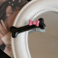 Close-up of the black Bowtiful Bones Hair Clip, featuring a glossy bone-shaped design with a pink bow accent.