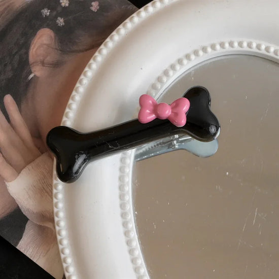 Close-up of the black Bowtiful Bones Hair Clip, featuring a glossy bone-shaped design with a pink bow accent.