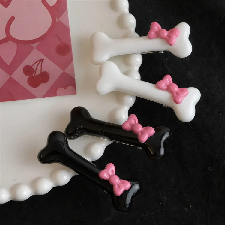 Flat lay of black and white Bowtiful Bones Hair Clips on a decorative plate, featuring glossy bone-shaped designs with pink bow accents. 