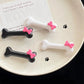 Flat lay of black and white Bowtiful Bones Hair Clips arranged on a plate, featuring glossy bone-shaped designs with pink bow accents.