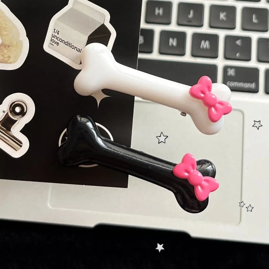 Black and white Bowtiful Bones Hair Clips displayed together, featuring glossy bone-shaped designs with pink bow accents.