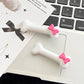 White Bowtiful Bones Hair Clip displayed on a flat lay, showcasing the glossy bone-shaped design and pink bow accent.