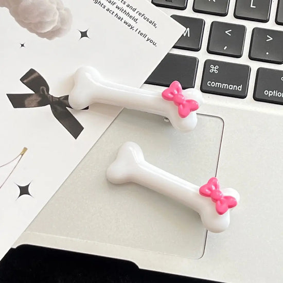 White Bowtiful Bones Hair Clip displayed on a flat lay, showcasing the glossy bone-shaped design and pink bow accent.