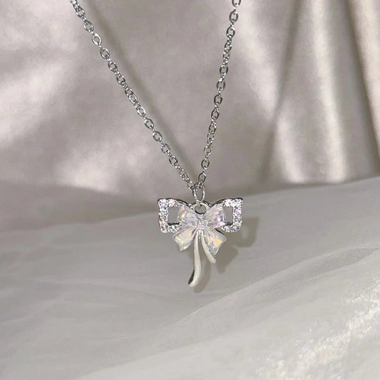 The Celestial Ribbon Bow Necklace, a silver crystal bow pendant necklace, displayed above soft white satin.