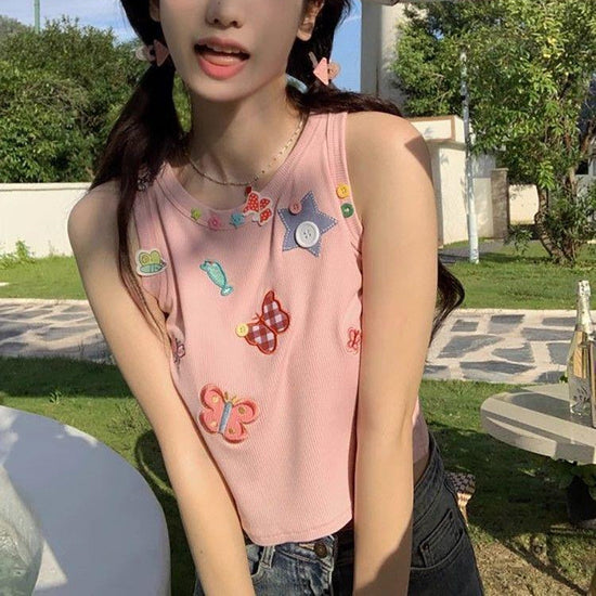 Model wearing the dusty pink Charm Collector Tank with denim shorts in an outdoor seated pose.