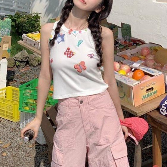 Full outfit view of a model wearing the white Charm Collector Tank with pink cargo pants at a fruit stand.