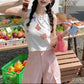 Standing model wearing the white Charm Collector Tank with pink pants beside market crates.