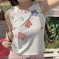 Model wearing the white Charm Collector Tank with colorful butterfly, star, animal, and button embellishments outdoors.