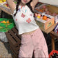 Model wearing the white Charm Collector Tank with pink cargo pants and one arm raised outdoors.