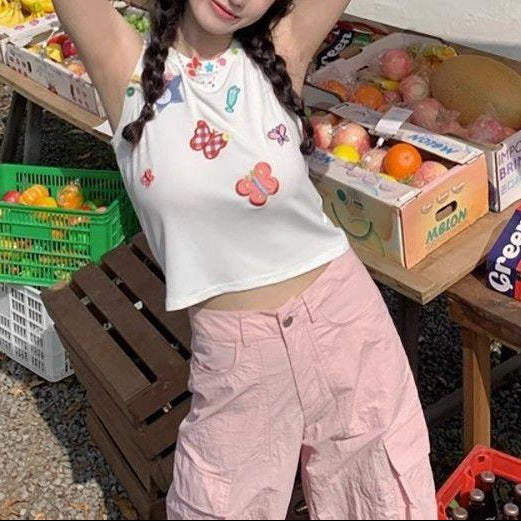 Model wearing the white Charm Collector Tank with pink cargo pants and one arm raised outdoors.