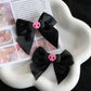 Creep It Cute Hair Bows — Pair of black skull hair bows on a white flower-shaped tray with pastel paper backdrop.