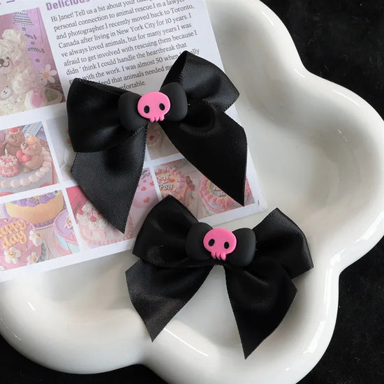 Creep It Cute Hair Bows — Pair of black skull hair bows on a white flower-shaped tray with pastel paper backdrop.