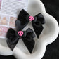 Creep It Cute Hair Bows — Pair of black satin hair bows with pink skull centers on a white flower-shaped tray.