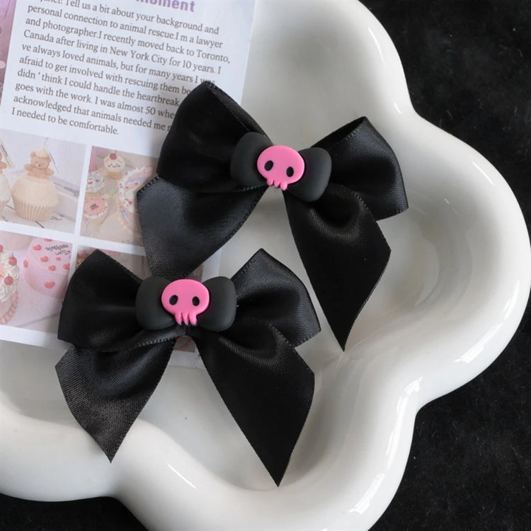 Creep It Cute Hair Bows — Pair of black satin hair bows with pink skull centers on a white flower-shaped tray.