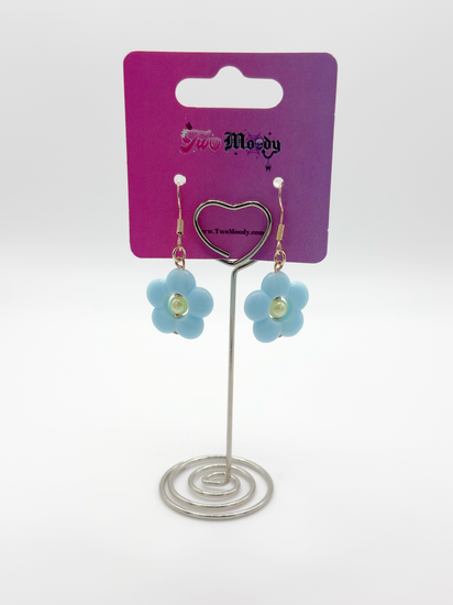 The Daisy Sky Earrings displayed on a card, highlighting the pastel blue flower design and delicate details.