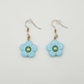 The Daisy Sky Earrings featuring soft blue daisy charms with a glossy finish in a lightweight, dreamy design.