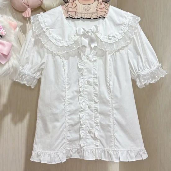 The Darling Honey Bear Blouse in white on a hanger, showcasing lace collar and ruffle trim.