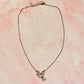 Flat lay of the Daydream Bow Necklace on pink marble background, highlighting bow charm