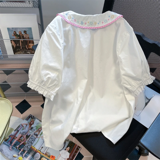 Back flat lay of the Doodle Darling Collar Blouse in white with pastel embroidered collar, pink gingham trim, and puff sleeves