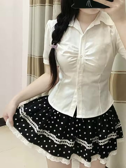 Model wearing the Dotted Doll Lace Skort with a fitted white button-up blouse while holding out the tiered hem.