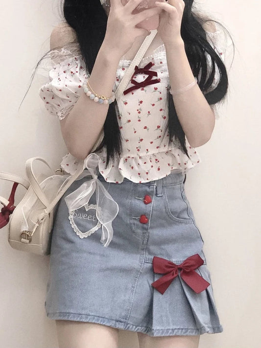 Model wears the Dual Darling Denim Skirt, showing off its half-pleated silhouette with an added red bow, lace heart embroidery, and heart-shaped buttons
