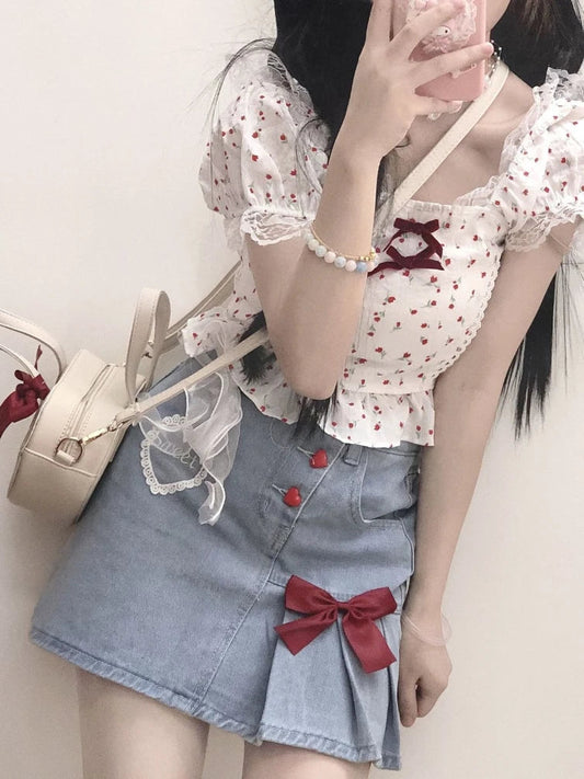 The Dual Darling Denim Skirt styled with a floral print blouse, highlighting the asymmetrical pleats, heart buttons, and red bow