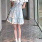 A model wearing the mini Ethereal Flower Princess Dress off the shoulder, showcasing its short puffed sleeves, a square neckline, lace detailing, and bow embellishment at the front.