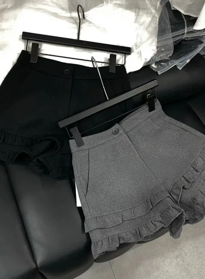 Frill Rush Layered Shorts in black and gray displayed on a hanger and laid on a couch