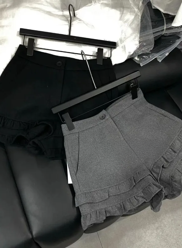 Frill Rush Layered Shorts in black and gray displayed on a hanger and laid on a couch