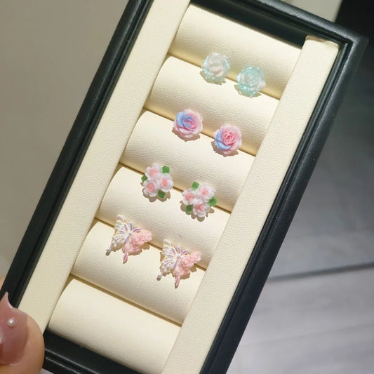 Garden Party Pastel Earrings displayed in a black and beige leather tray, featuring four pastel floral and butterfly designs.