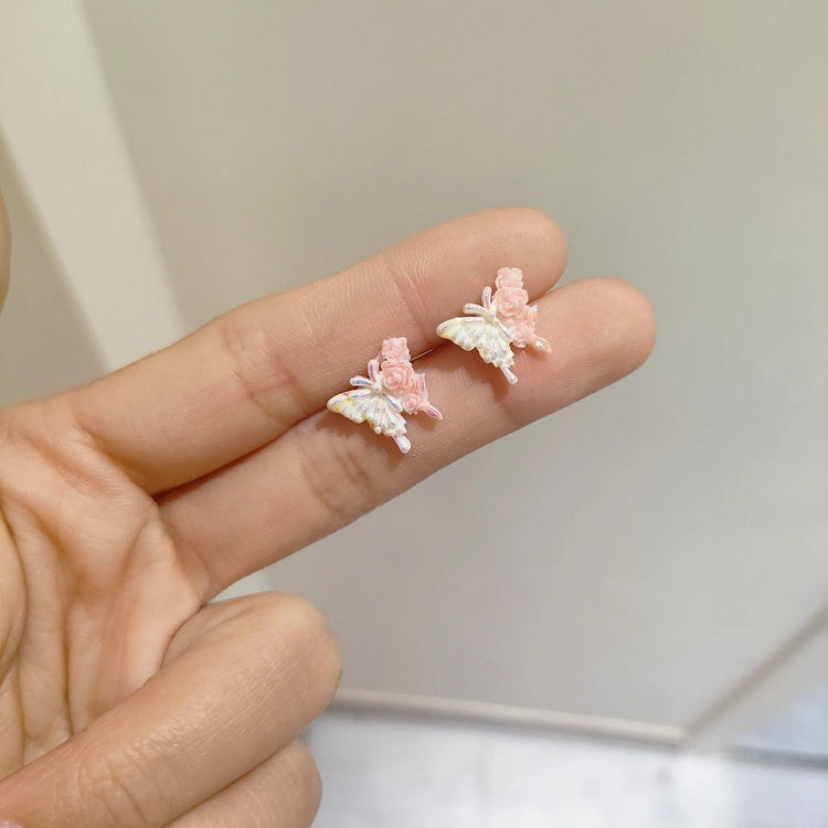 Pastel pink and white butterfly earrings with miniature roses, held gracefully in between two fingers from the Garden Party Pastel Earrings set.