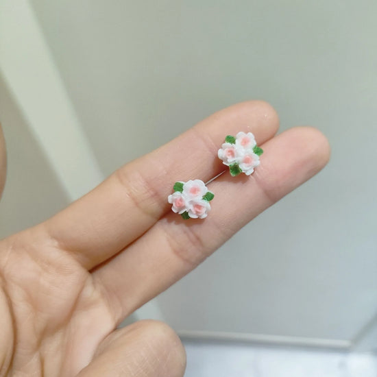 Pink and white clustered camellia flower earrings with green leaf accents, held gracefully in between two fingers from the Garden Party Pastel Earrings set.