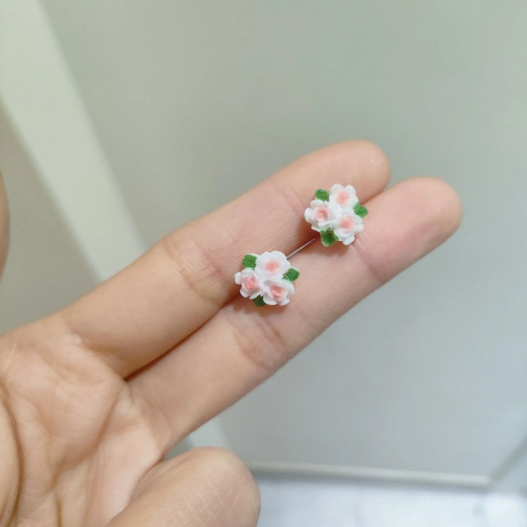 Pink and white clustered camellia flower earrings with green leaf accents, held gracefully in between two fingers from the Garden Party Pastel Earrings set.