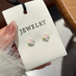 Close-up of pastel pink, white, and blue rose bouquet earrings with green leaf accents, displayed on a cream jewelry card from the Garden Party Pastel Earrings.
