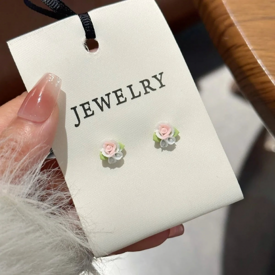 Close-up of pastel pink, white, and blue rose bouquet earrings with green leaf accents, displayed on a cream jewelry card from the Garden Party Pastel Earrings.