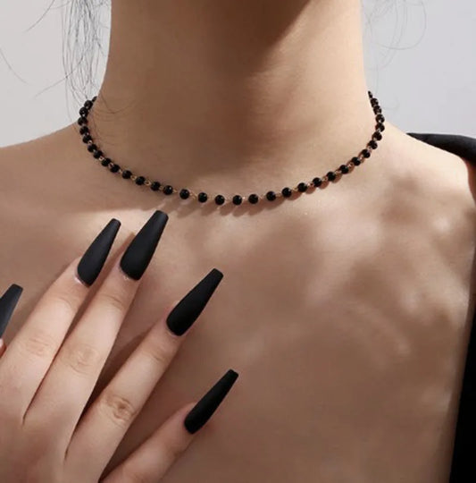 A model wearing the Inkdrop Beaded Choker, a delicate black beaded choker, with long black nails against a gray background.