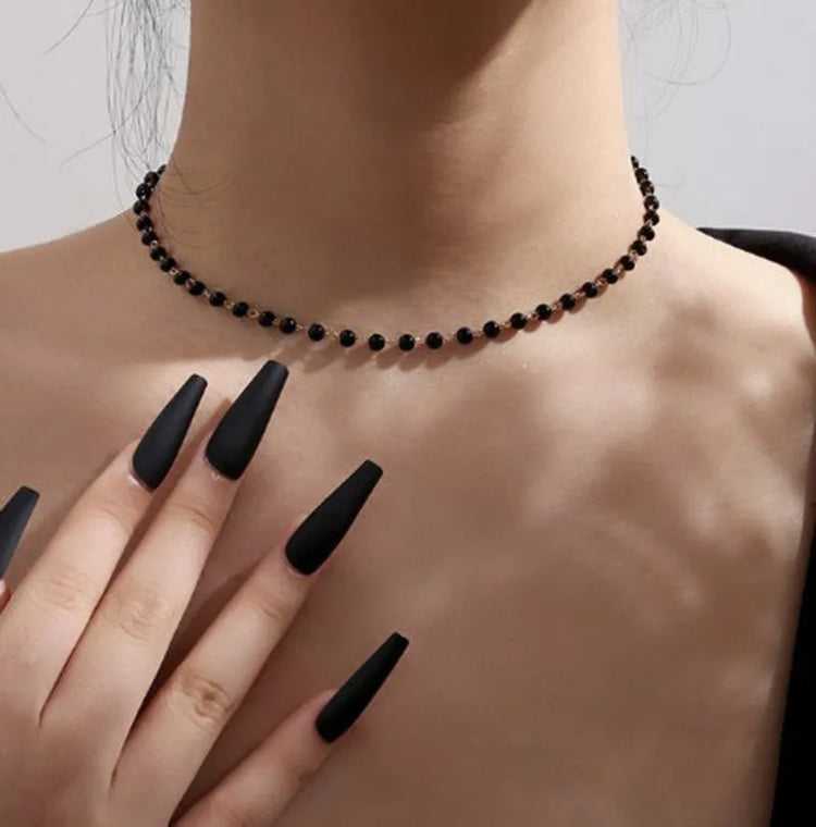A model wearing the Inkdrop Beaded Choker, a delicate black beaded choker, with long black nails against a gray background.