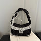 The Lacy Dotling Purse, a black, polka-dot, lace-trimmed purse, displayed on a black table atop a book.