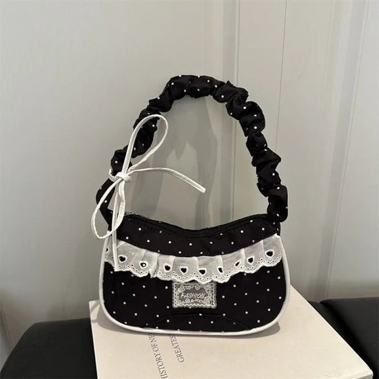 The Lacy Dotling Purse, a black, polka-dot, lace-trimmed purse, displayed on a black table atop a book.