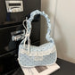 The Lacy Dotling Purse, a light-blue, polka-dot, lace-trimmed purse, displayed on a black table atop a book.