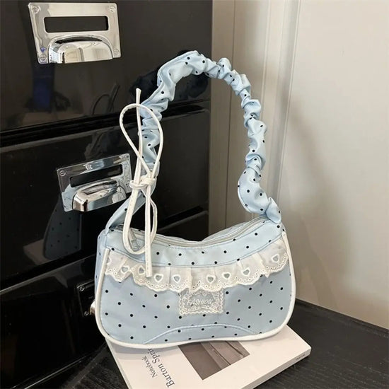The Lacy Dotling Purse, a light-blue, polka-dot, lace-trimmed purse, displayed on a black table atop a book.