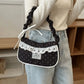 A model carrying the black Lacy Dotling Purse, a polka-dot lace-trimmed purse, while wearing a casual cream sweater and jeans.