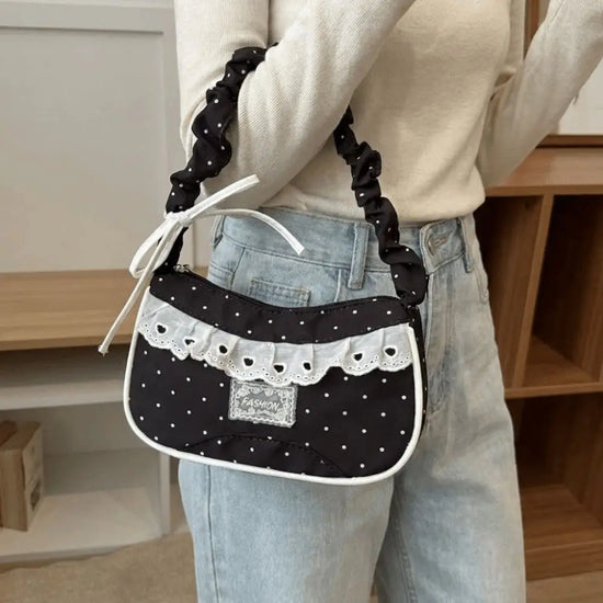 A model carrying the black Lacy Dotling Purse, a polka-dot lace-trimmed purse, while wearing a casual cream sweater and jeans.