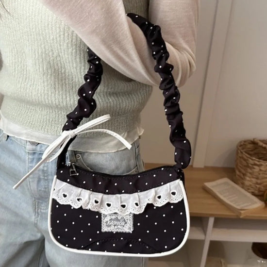 A model holding the black Lacy Dotling Purse, a polka-dot lace-trimmed purse, by the gathered handle.