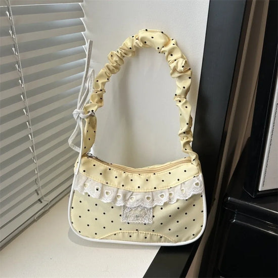 The Lacy Dotling Purse, a yellow, polka-dot, lace-trimmed purse, displayed on a white windowsill.