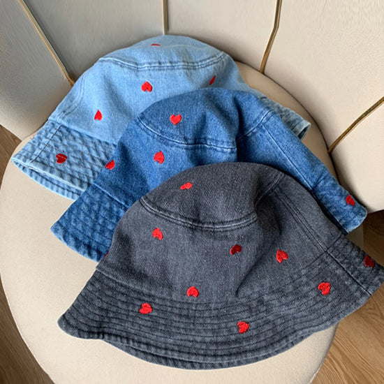 Different color variations of the Love Stitch Denim Bucket Hat arranged together, showing light and dark denim options with heart embroidery.