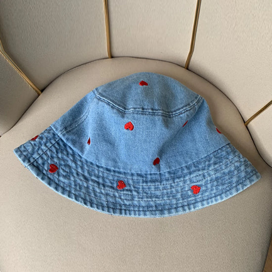 The Love Stitch Denim Bucket Hat in light blue denim, displayed flat to highlight the scattered embroidered heart details.