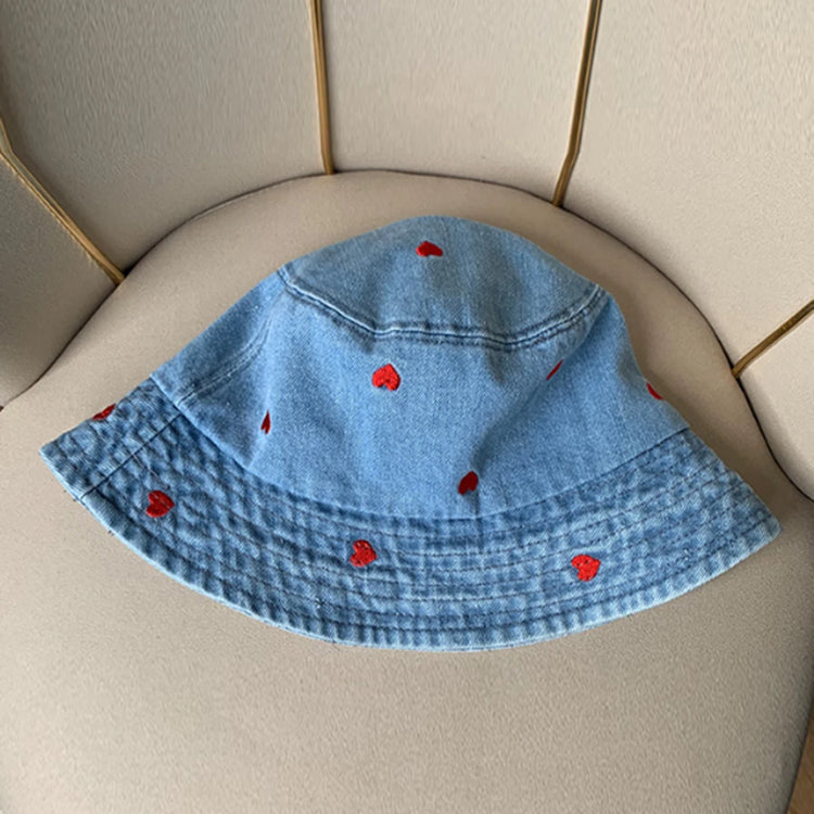 The Love Stitch Denim Bucket Hat in light blue denim, displayed flat to highlight the scattered embroidered heart details.