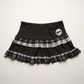 Front flat lay of the Lovestruck Skull Skort, featuring gray plaid trim and a heart-eyed skull patch.