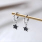 The Midnight Star Drop Earrings, black star drop hoop earrings, hanging from a gold display rod.